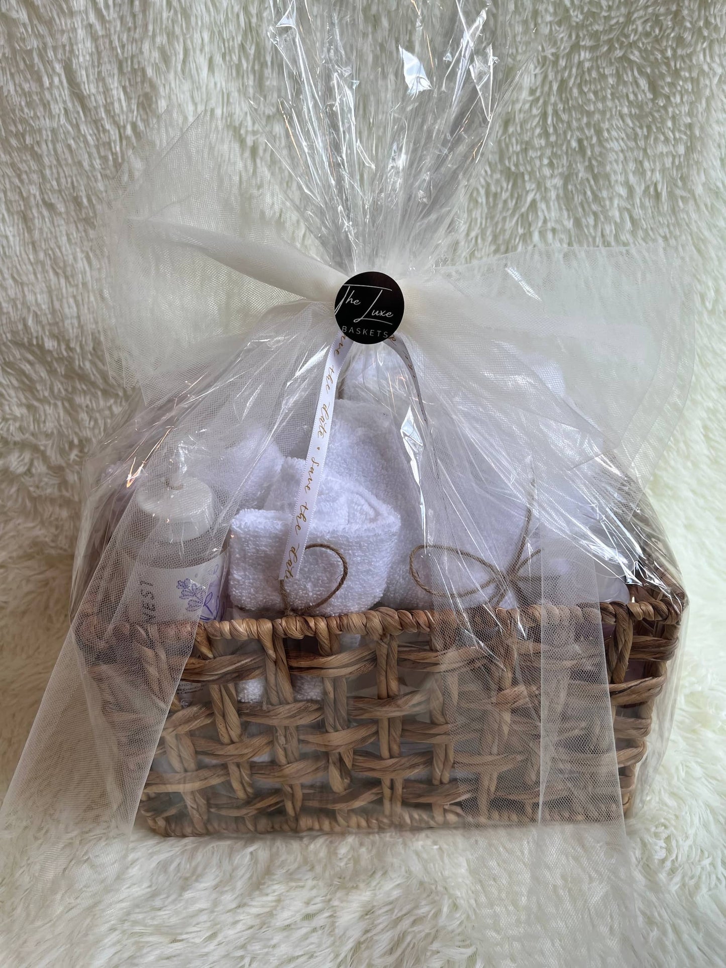 Gift basket for couple, wrapped in cellophane with a ribbon on a textured white background.