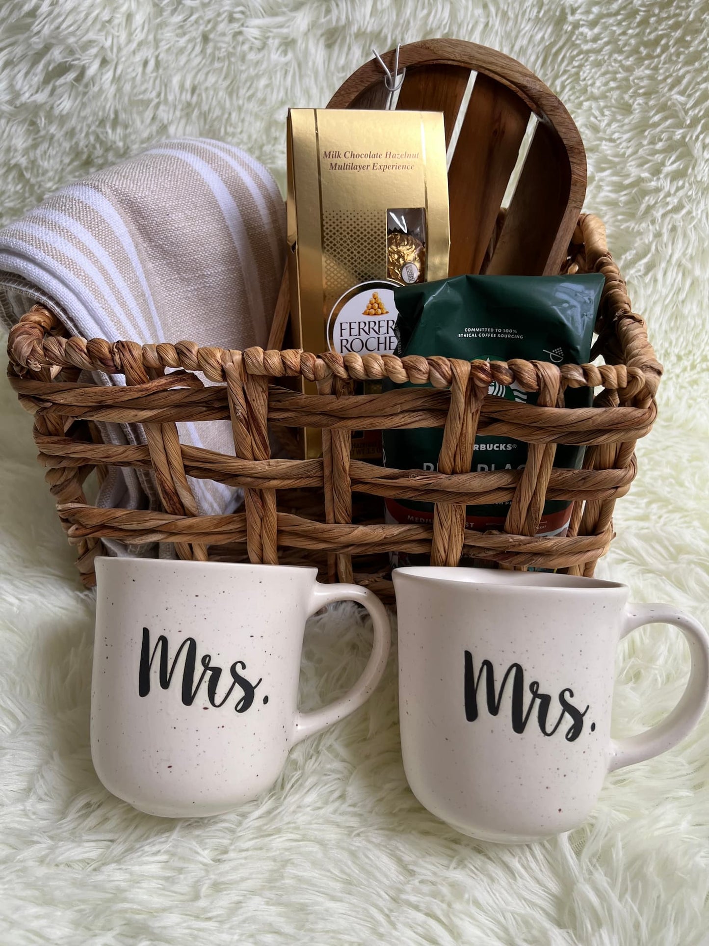 Basket with snacks and two 'Mrs.' mugs on a soft surface