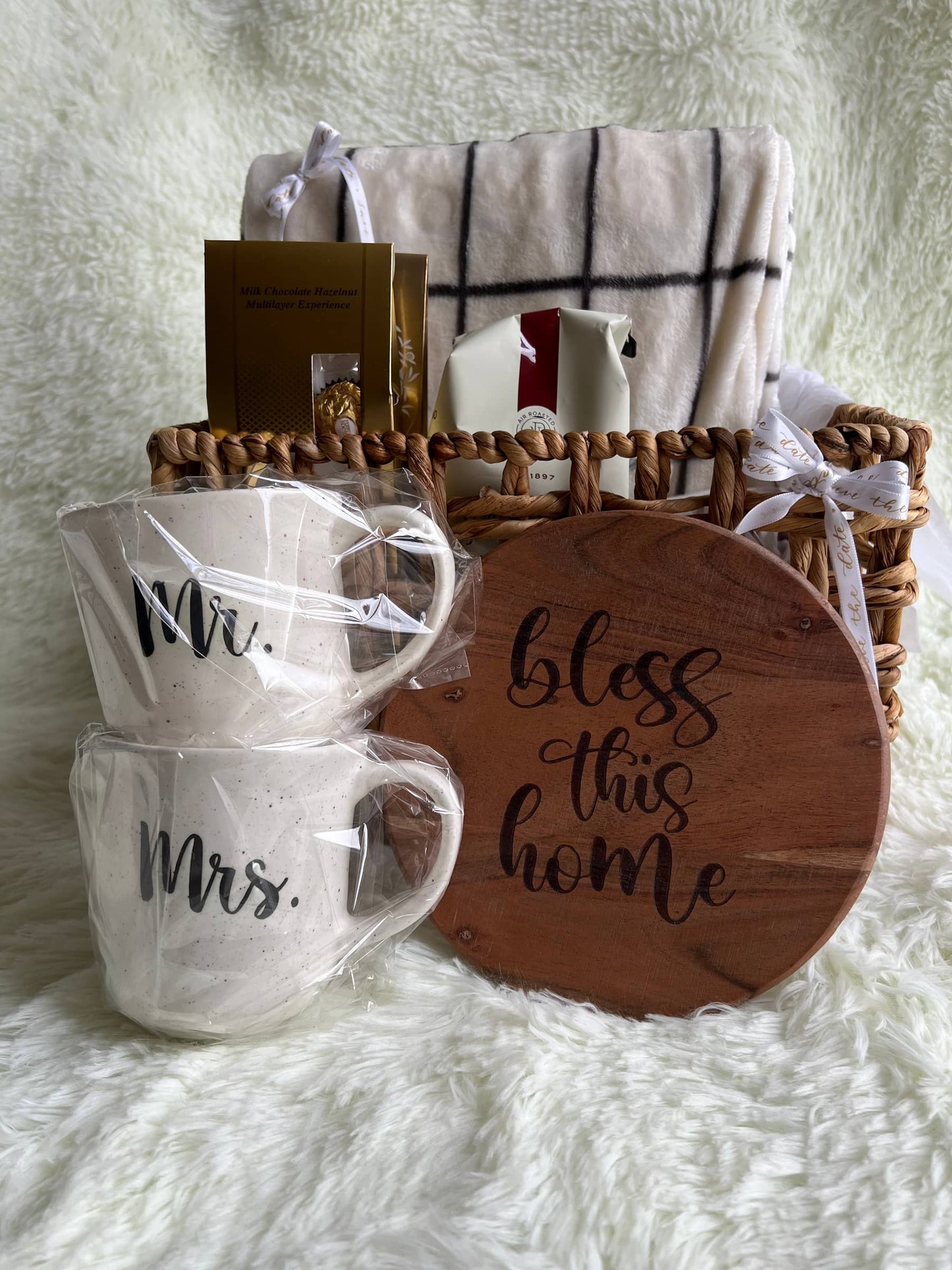 Gift basket with 'Mr. Mrs.' mugs, wooden sign, and blanket on a white surface.