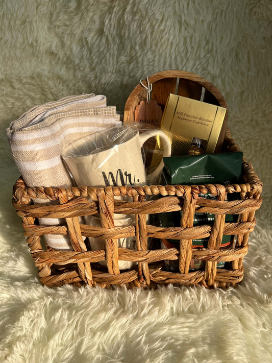 Wicker basket with kitchen products including a coffee, a mug set, and towels on a textured surface.