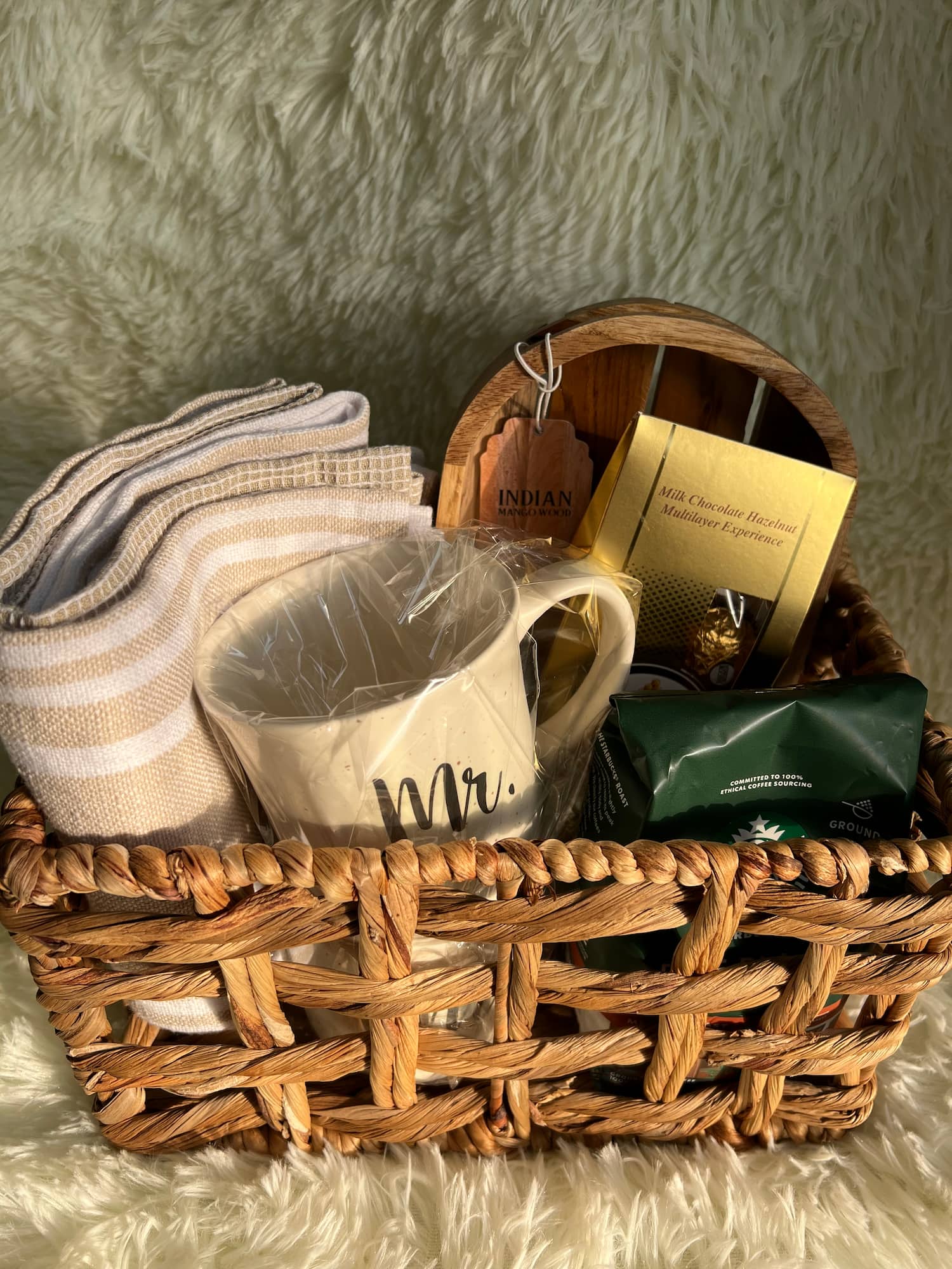 Rattan basket with a mug set, kitchen towels, aromatic coffee, and other gift items in the morning sun