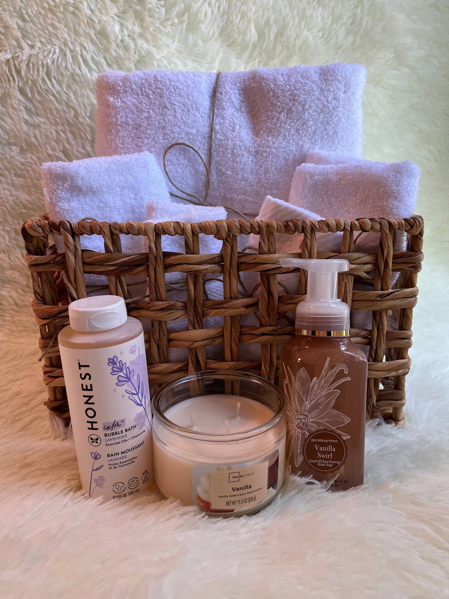Bath products including a bubble bath bottle, foaming soap, and a candle in front of a basket with towels.