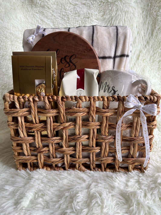 Woven basket with decorative items including a wooden sign, plates, and books on a white fluffy surface.